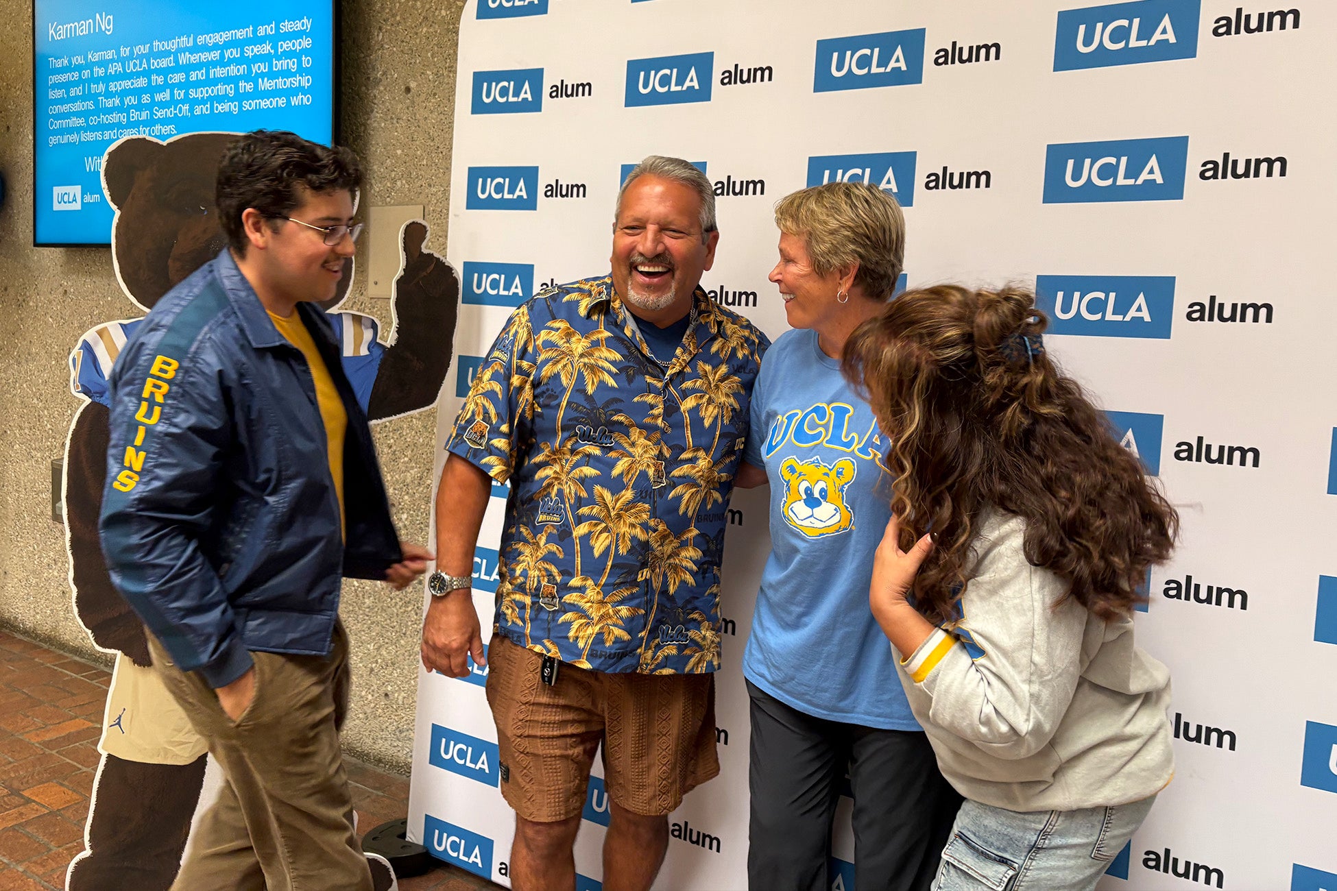 Group of alumni smiling and talking in front of a UCLA Alumni photo backdrop.