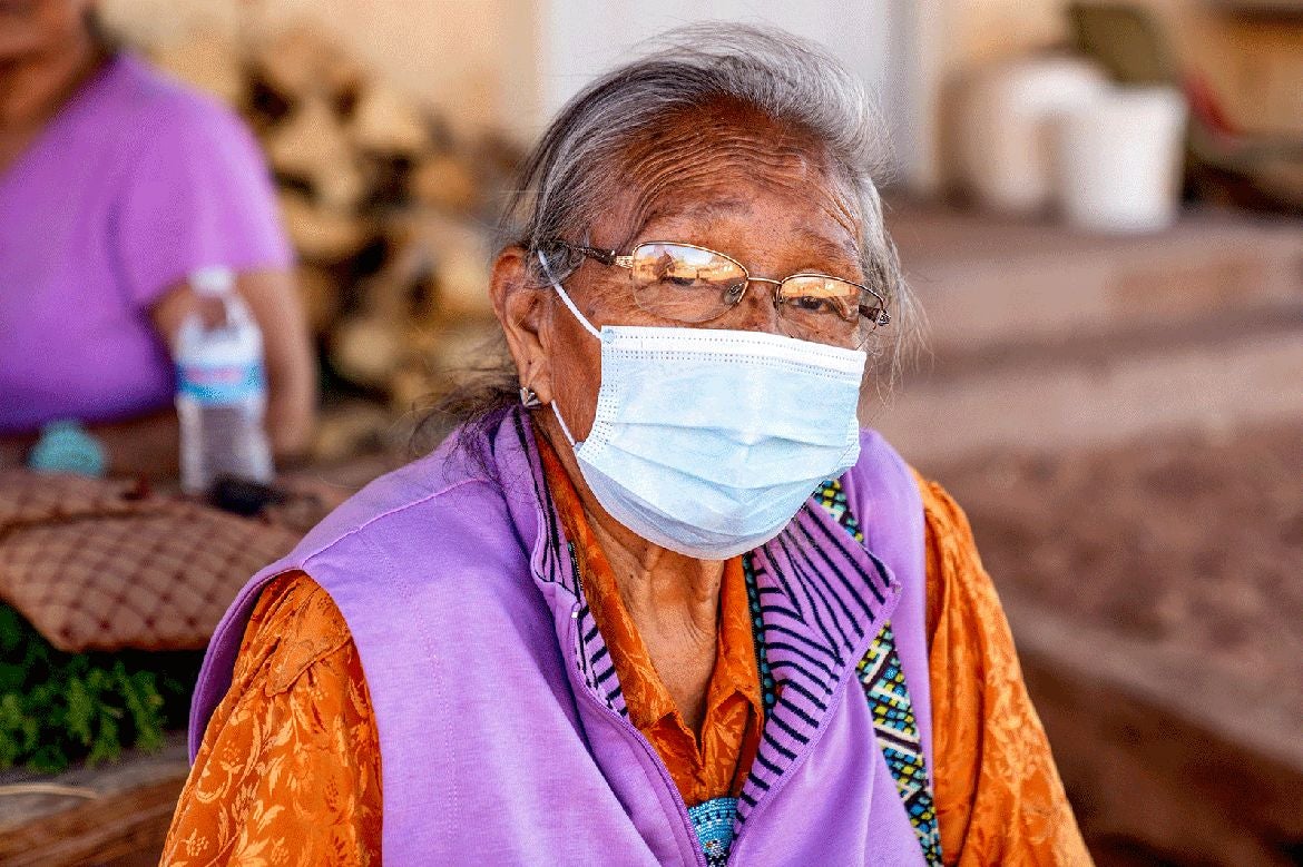 Elderly indigenous woman in orange and purple wearing surgical mask