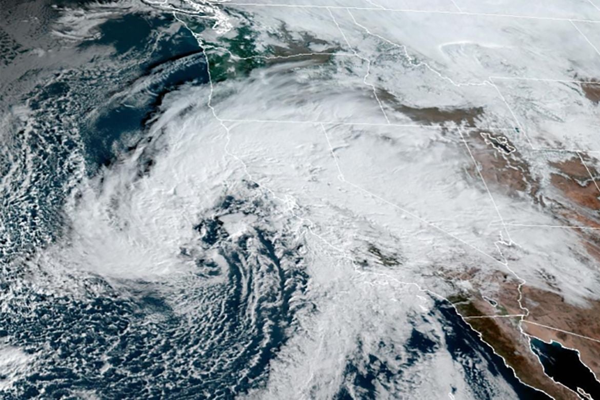 Satellite image showing a large swirling storm system with dense white clouds stretching across the western United States and the Pacific Ocean.