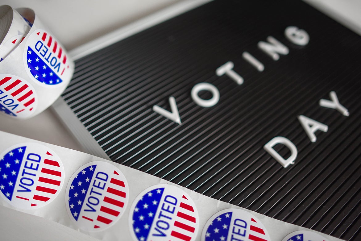 Red, white and blue "I Voted" stickers next to a black-and-white "Voting Day" sign.